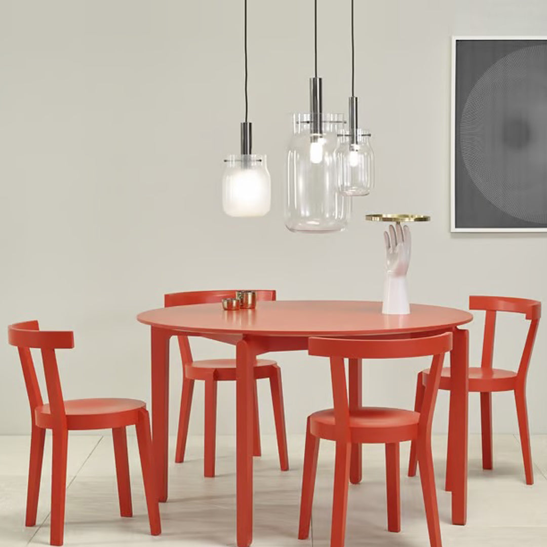 Stylish round red dining table with matching chairs, complemented by clear glass pendant lights. Modern and vibrant design.