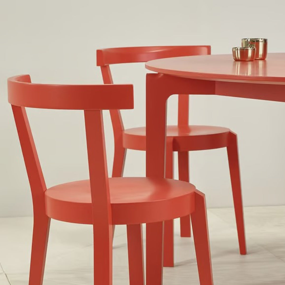 Bright coral dining set with a round table and matching chairs, featuring smooth, modern lines and a minimalist design.
