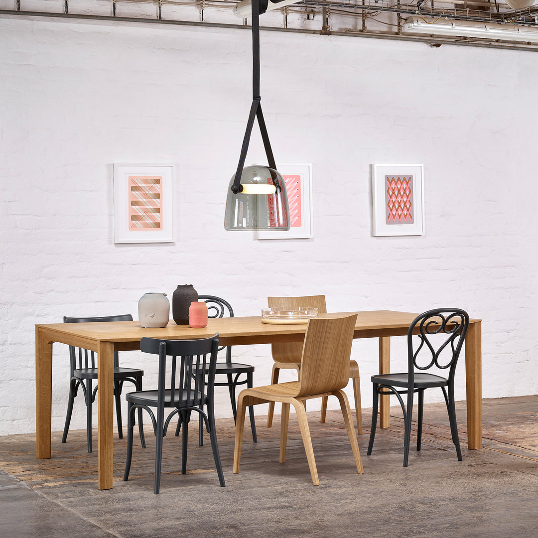 Wooden dining table with black, natural, and patterned chairs. Artwork features pink and geometric designs on white walls.