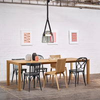 Wooden dining table with black, natural, and patterned chairs. Artwork features pink and geometric designs on white walls.