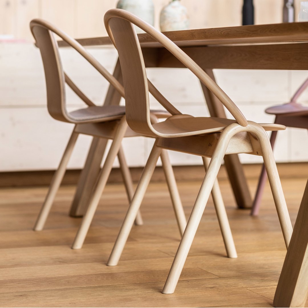 Natural wood chairs with a light beige finish, featuring a minimalist design and curved backrest, set against a warm wooden floor.