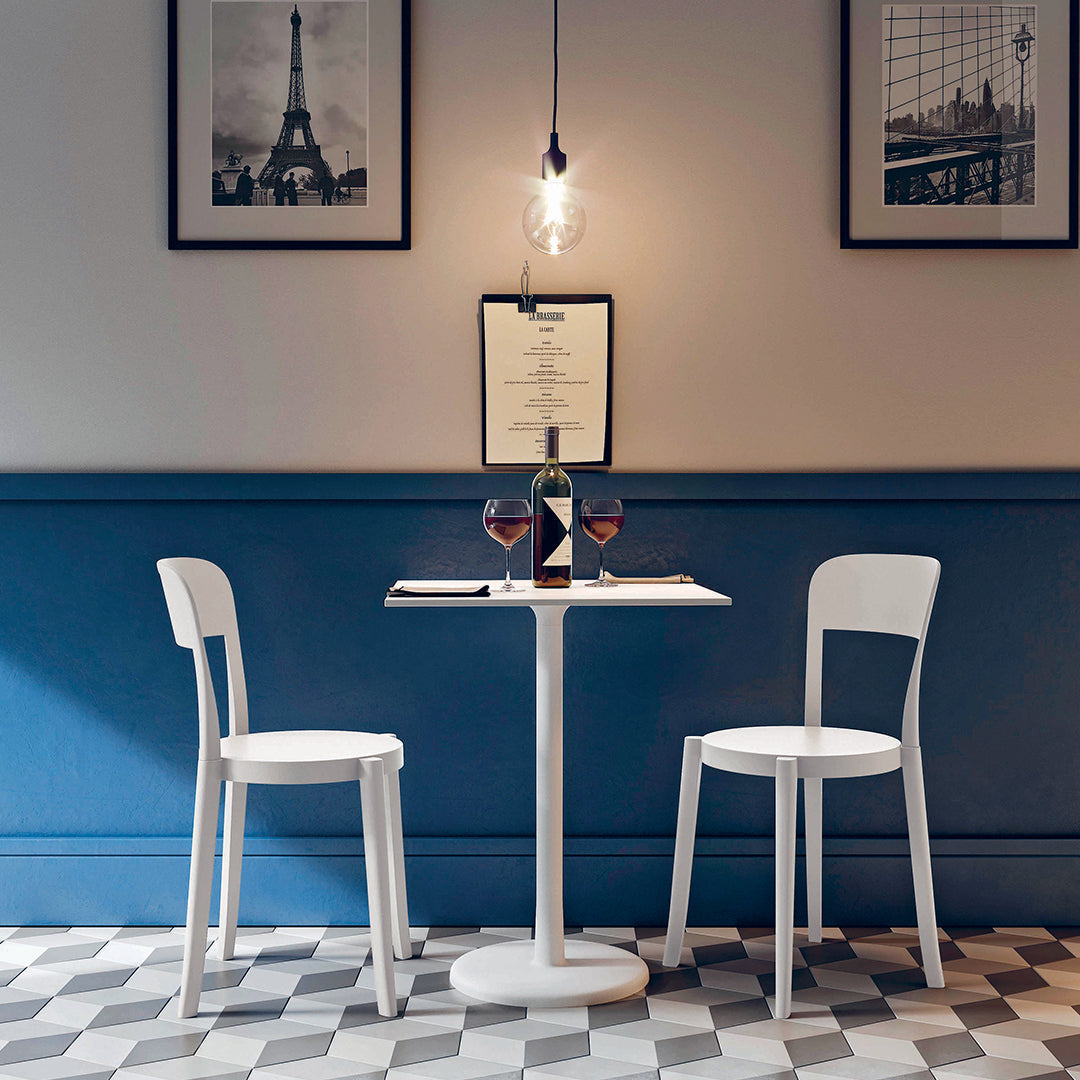 White chairs and table against a dark blue wall with a checkered black-and-white floor pattern. Elegant and modern design.