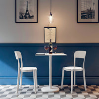 White chairs and table against a dark blue wall with a checkered black-and-white floor pattern. Elegant and modern design.