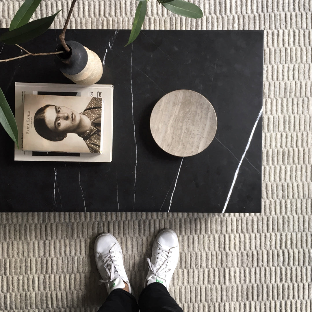 Black marble table with white veining, textured beige rug, and minimalistic decor in neutral tones.
