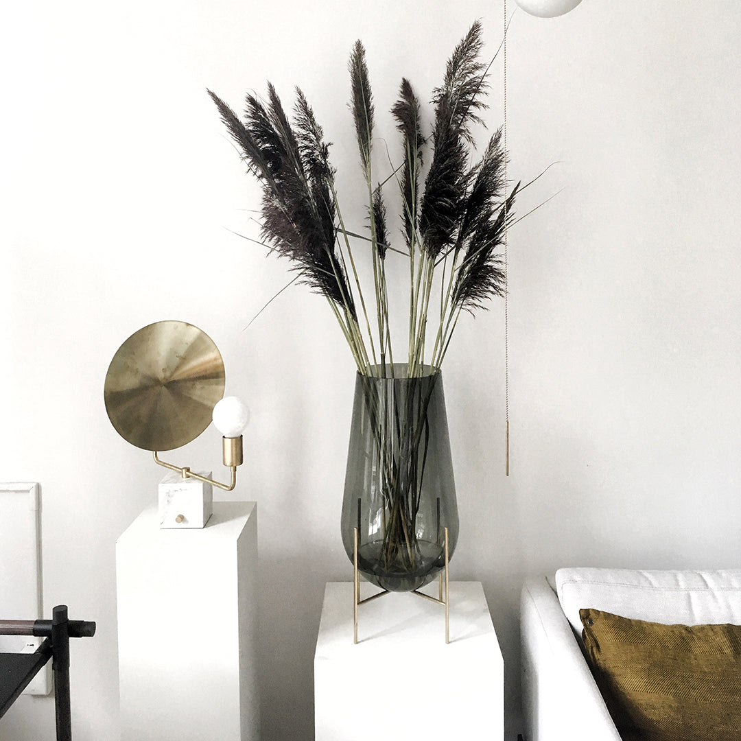 Gray glass vase filled with dark pampas grass, set against a minimalistic white background. Modern and elegant design.