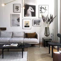 Modern living room with neutral tones, textured beige rug, black tables, and wall art in monochrome and gold accents.