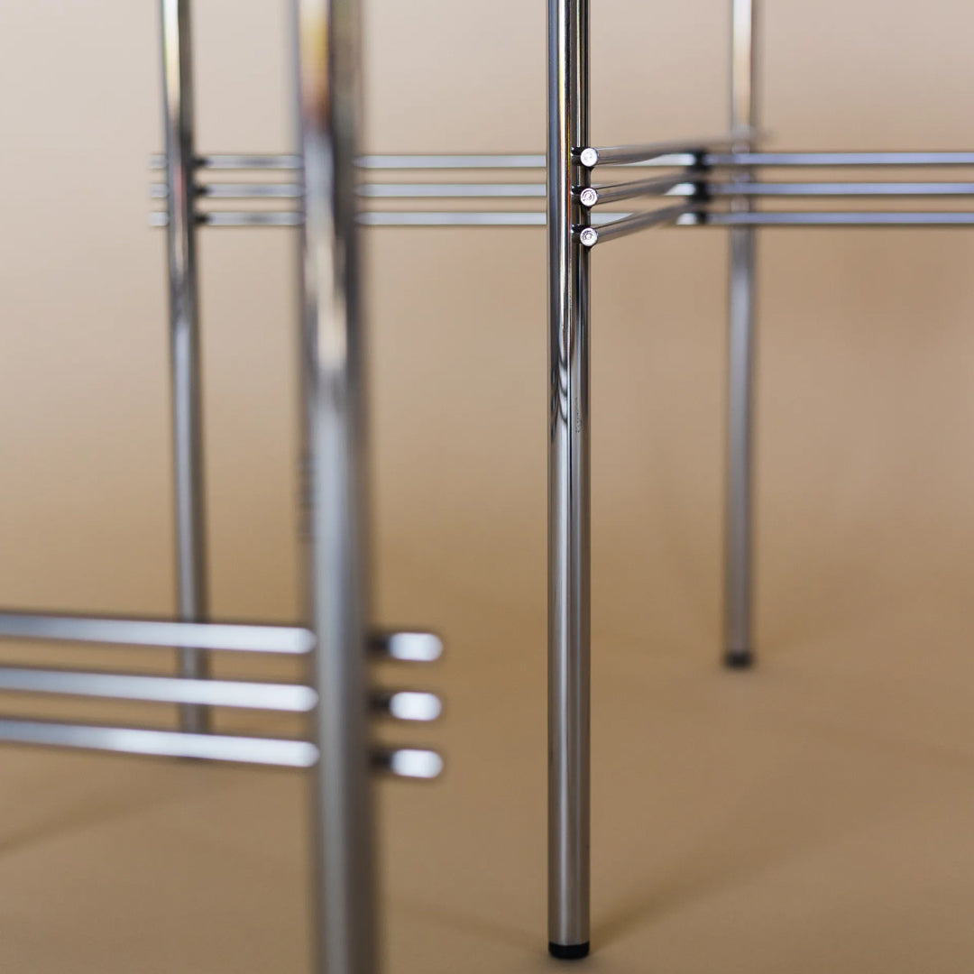 Chrome metal chair frame with sleek lines and a modern design, set against a soft beige background.