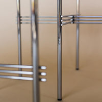 Chrome metal chair frame with sleek lines and a modern design, set against a soft beige background.
