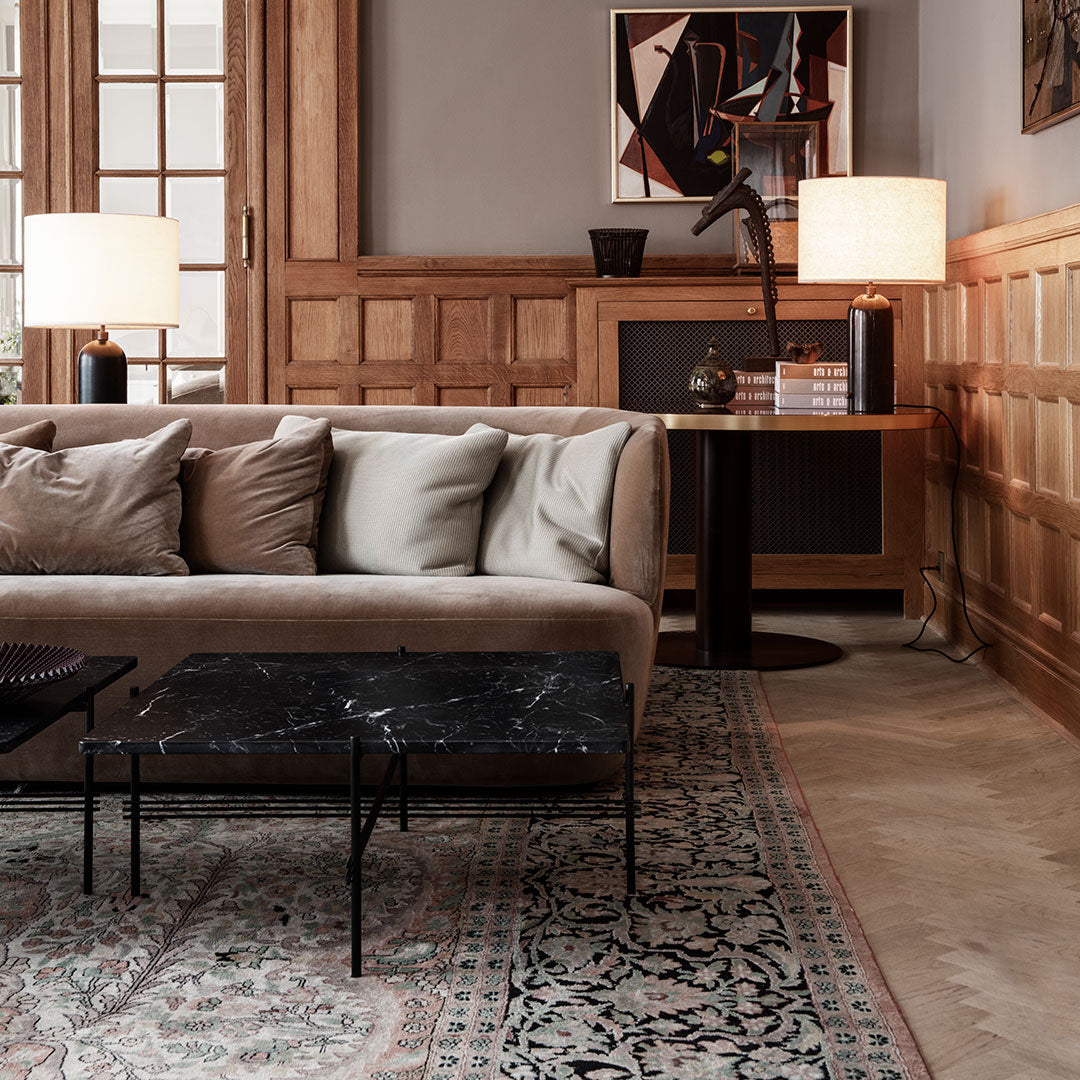 Beige sofa with gray cushions on a patterned rug featuring intricate floral designs. Black marble coffee table accent.