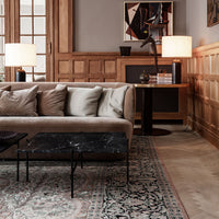 Beige sofa with gray cushions on a patterned rug featuring intricate floral designs. Black marble coffee table accent.