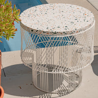 Round terrazzo table with a speckled white top and geometric white metal base, ideal for modern outdoor settings.