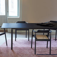 Modern black dining table with minimalist design, paired with beige accent chairs and a soft pink area rug.