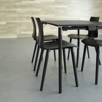 "Modern black dining table with sleek black chairs, set against a light wood and grey background."