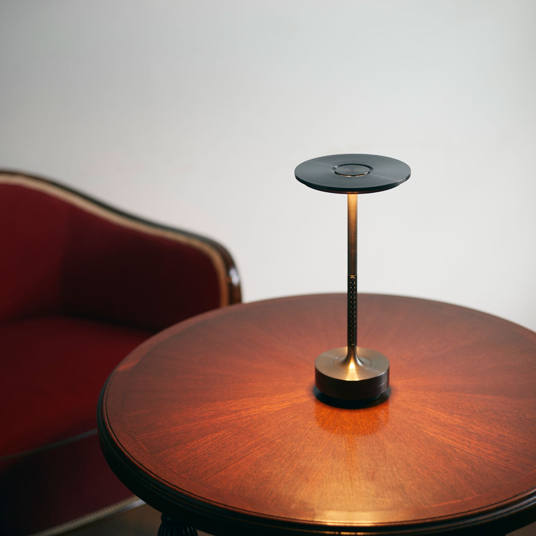 Sleek black lamp with gold accents on a polished wooden table, paired with a rich burgundy chair.
