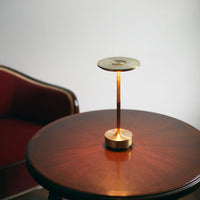 Gold lamp on a wooden table with a rich, dark brown finish and a deep red upholstered chair in the background.