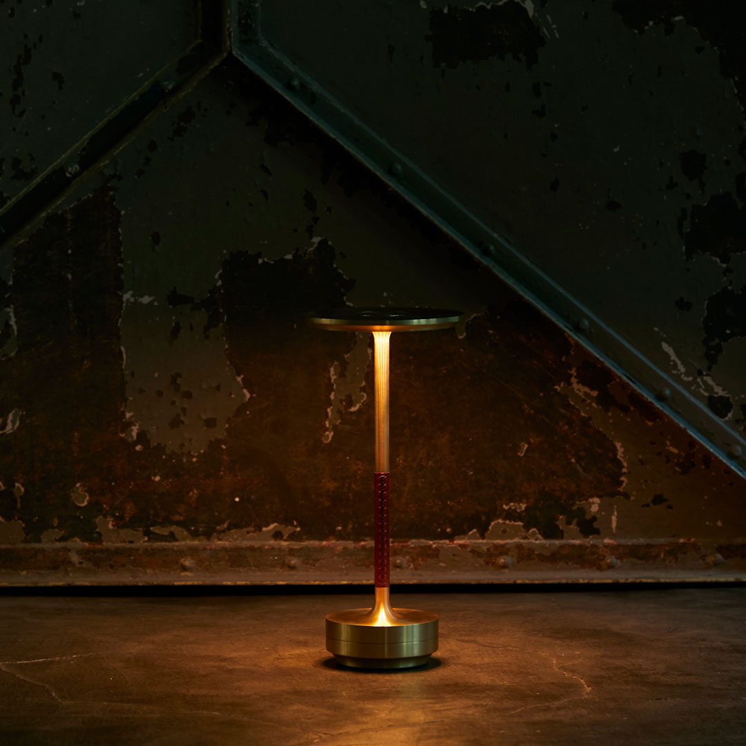 Sleek brass lamp with a red handle, set against a dark, textured backdrop of green and rust colors.