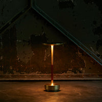Sleek brass lamp with a red handle, set against a dark, textured backdrop of green and rust colors.