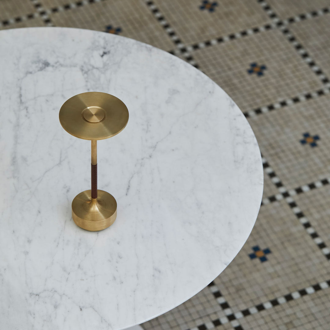 Brass lamp on a white marble table, with intricate patterned tiled flooring in muted tones and blue accents.