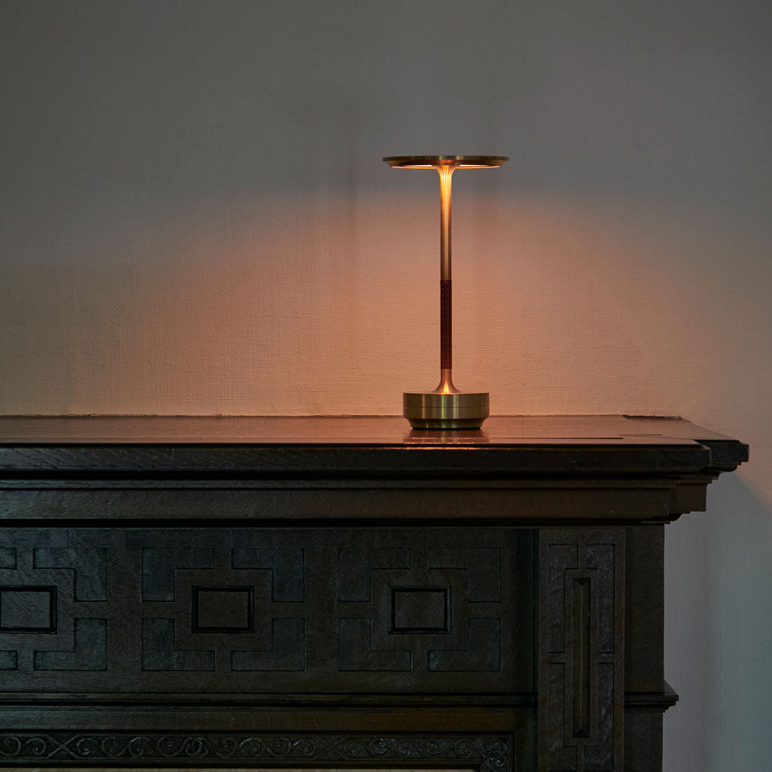 Brass and burgundy lamp with warm light, contrasting against a dark wooden surface and textured wall.