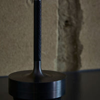 Black braided leather handle on a sleek, dark metallic base against a textured beige wall.