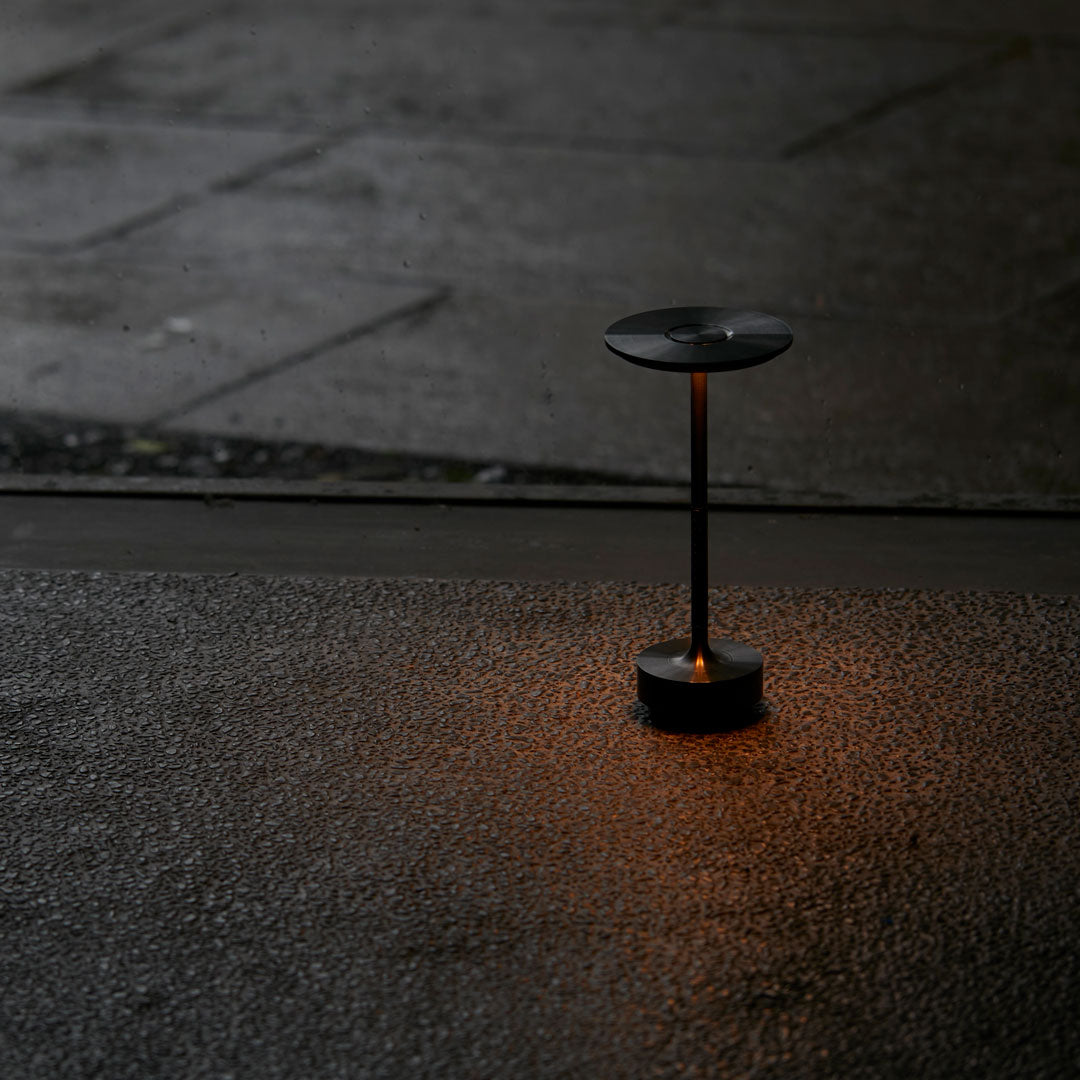 Sleek black lamp with warm orange glow on textured dark surface, creating a modern contrast in ambient lighting.