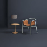 Modern chair with a woven orange seat, soft gray frame, paired with a light wooden side table and gray lampshade.