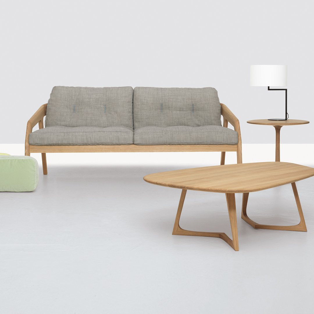 Gray sofa with wooden frame, light wood coffee table, modern lamp, and green accent chair on a minimalist white floor.