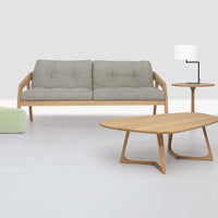 Gray sofa with wooden frame, light wood coffee table, modern lamp, and green accent chair on a minimalist white floor.