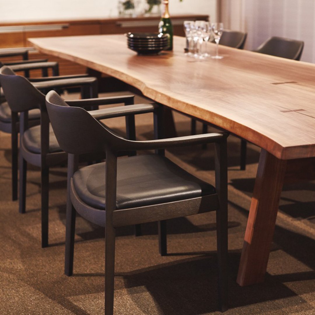 Brown velvet chair with a circular seat and backrest, metal frame, next to a white table in a warm, sunlit setting.