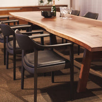 Brown velvet chair with a circular seat and backrest, metal frame, next to a white table in a warm, sunlit setting.