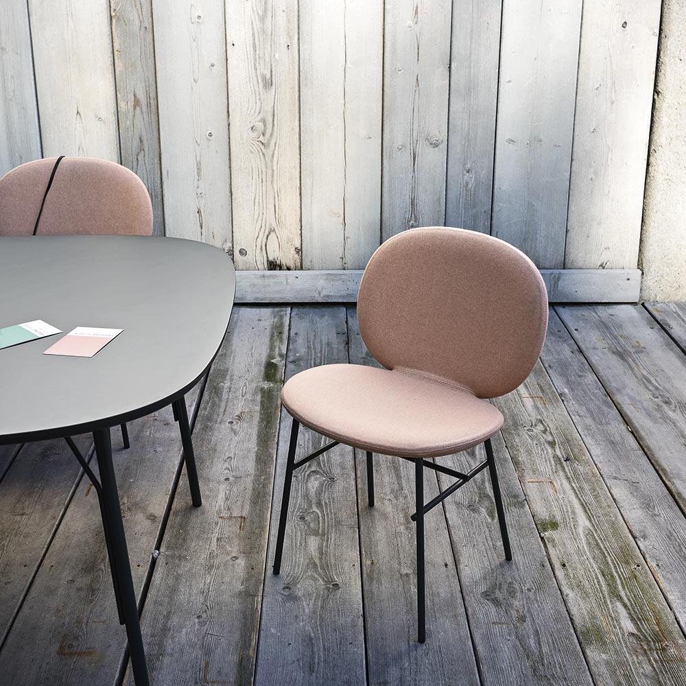 Blush pink upholstered chair with a smooth finish, paired with a sleek gray table against a rustic wooden backdrop.