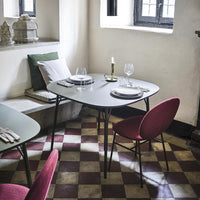 Green table with black legs, surrounded by burgundy chairs against a classic checkered floor in earthy tones.