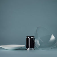 Clear glass bowl, sleek black separator, and white plate against a soft blue background, showcasing modern minimalist design.