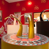 Gold and black accessory displays with intricate red and teal patterned bases on a vibrant red background.