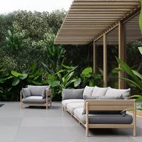 Modern outdoor sofa set with gray cushions and light wooden frames, surrounded by lush green foliage.