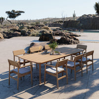 Wooden dining table with natural finish and beige cushions on light wooden chairs, set against a desert landscape.