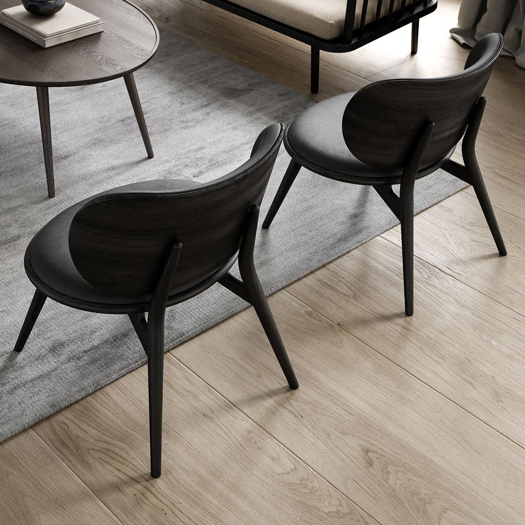 Elegant dark wood chairs with curved backs, set against a soft gray rug and light brown floor. Modern minimalist design.