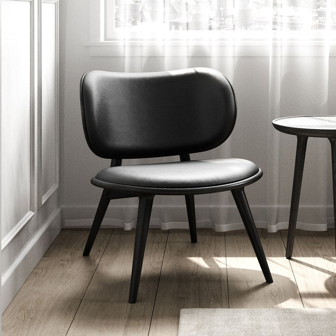 Black leather chair with a sleek, minimalist design and smooth, rounded patterns, set against a light, airy backdrop.