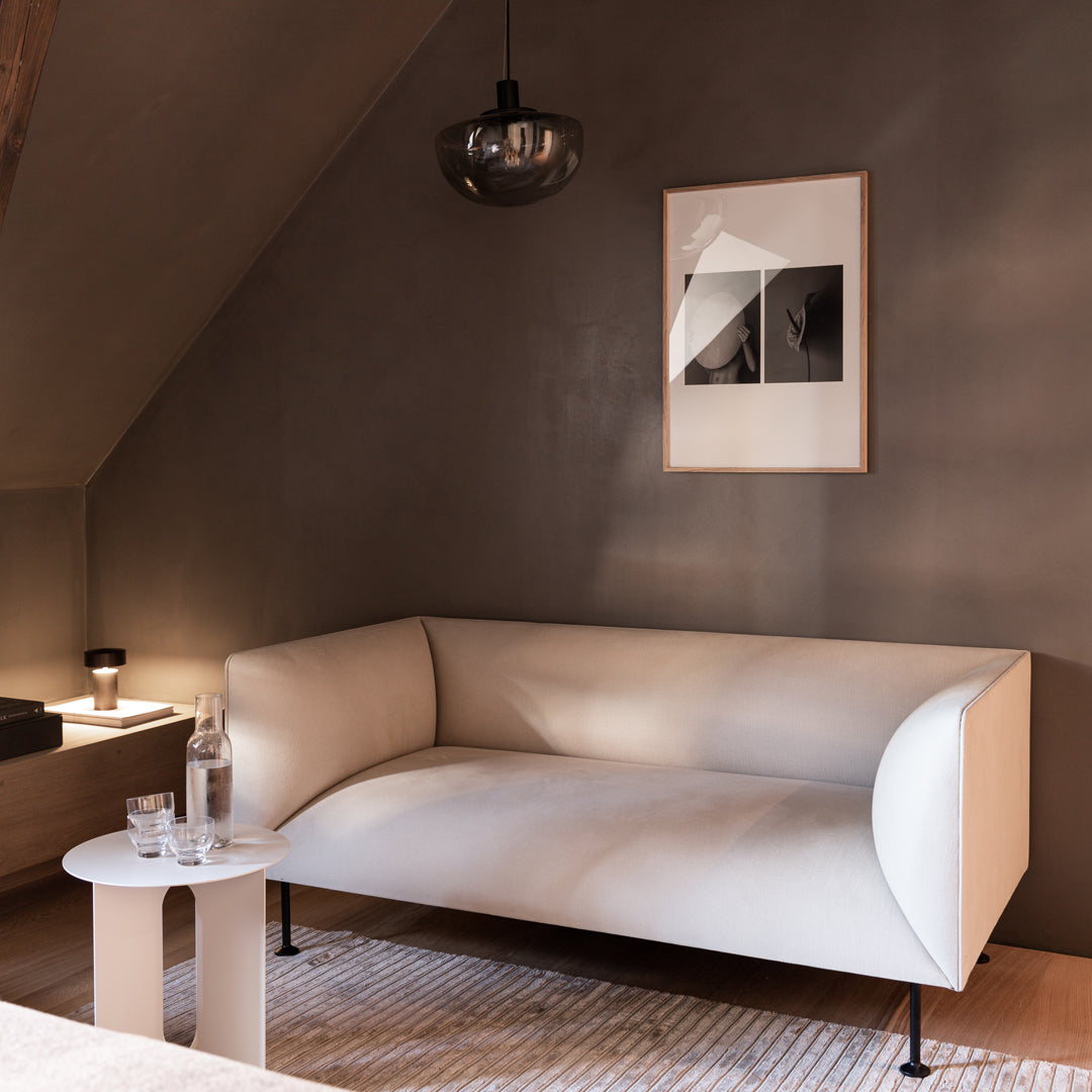 Stylish cream sofa with curved edges on a textured beige rug, complementing a neutral-toned wall and contemporary decor.