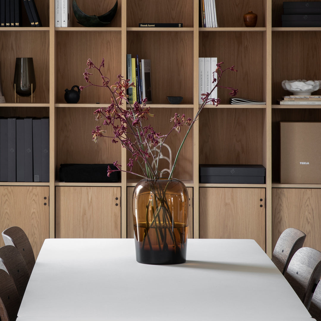 Amber glass vase with dark base, featuring purple floral accents, set against a modern wooden shelving unit.