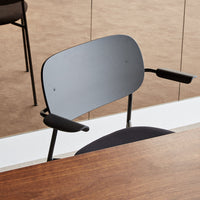 Black ergonomic chair with sleek curved backrest and armrests, set against a light brown background. Stylish and modern design.