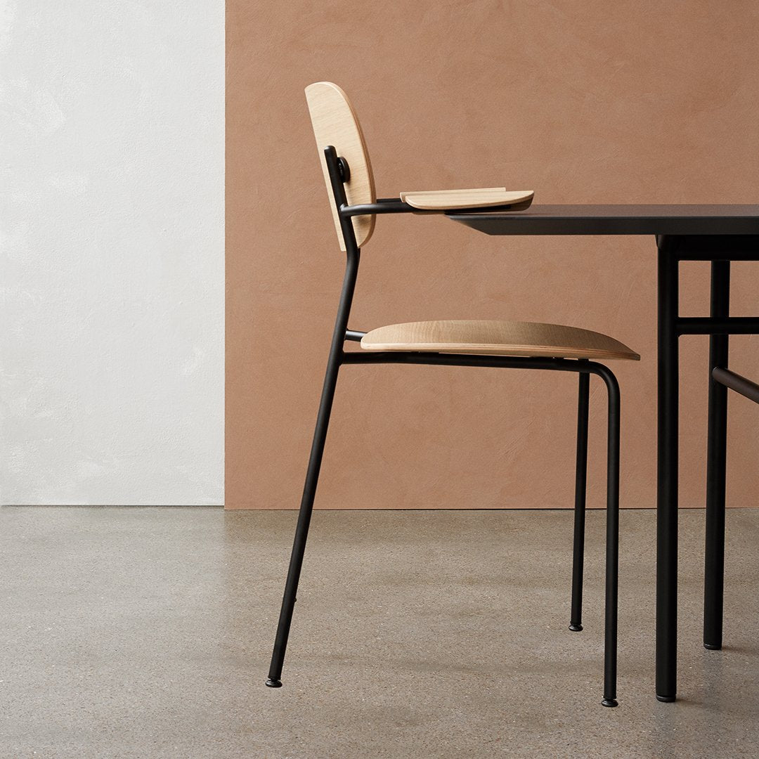 Light wooden chair with black metal legs against a textured beige wall and smooth concrete floor, sleek modern design.