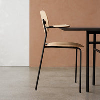 Light wooden chair with black metal legs against a textured beige wall and smooth concrete floor, sleek modern design.