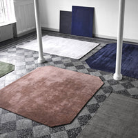 Variety of rugs in brown, gray, green, navy, and white on a patterned floor, showcasing modern geometric designs.