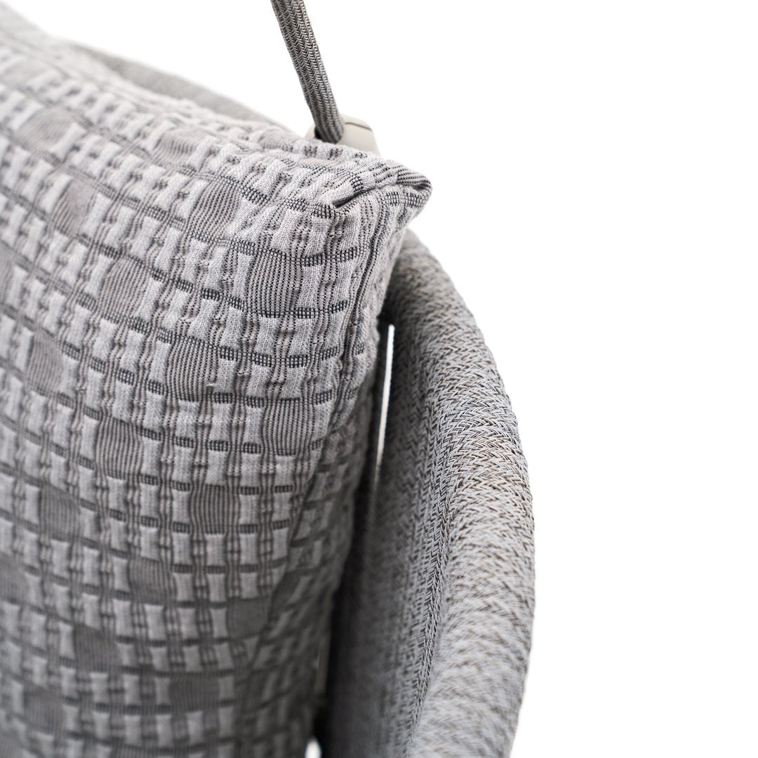 Gray woven cushion with a textured pattern, featuring a mix of check and dot designs, on a curved gray chair.
