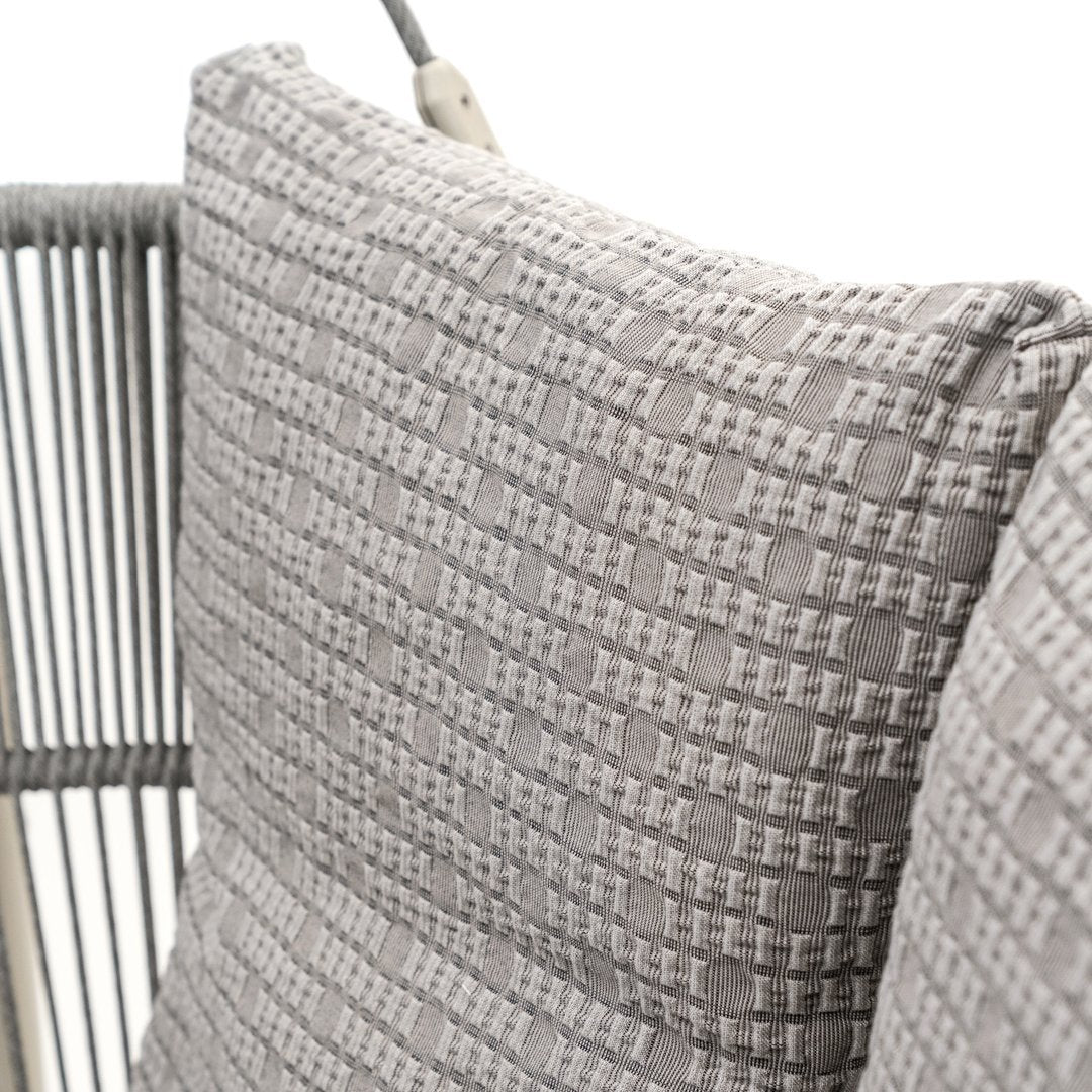 Gray textured pillow with a woven pattern, accented by a soft, neutral color palette on a stylish modern chair.