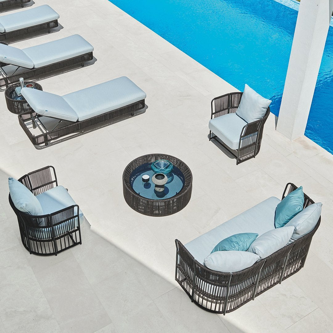 Outdoor seating set with a modern black wicker finish, light blue cushions, and a round glass-top coffee table.
