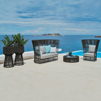 Black wicker patio furniture with light gray cushions and turquoise accent pillows, set against a tranquil blue ocean backdrop.