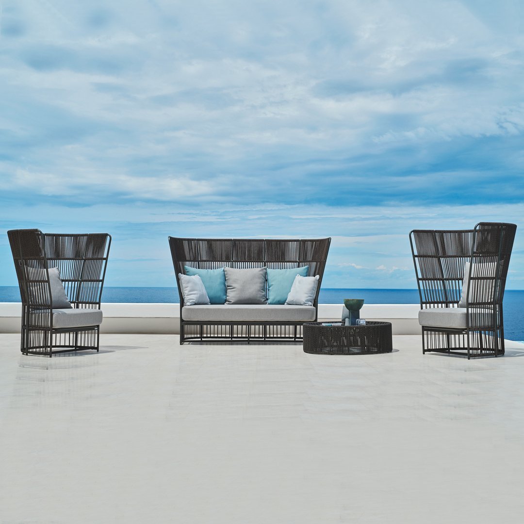 "Black wicker patio set with light blue cushions, showcasing a minimalist design against a serene ocean backdrop."
