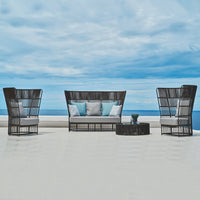 "Black wicker patio set with light blue cushions, showcasing a minimalist design against a serene ocean backdrop."